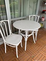Photo of the white bentwood patio furniture set showing 2 chairs and the matching round table on a wood patio floor.