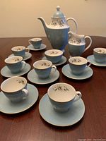 Full tea service set arranged together showing teapot, creamer, sugar container and 8 cups with saucers on a table.