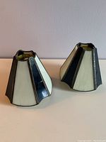 Two stained glass candle shades with alternating cream and black panels in brass framing, displayed side by side.