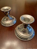 Pair of silver weighted candlesticks on a wooden surface showing overall design.
