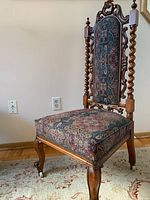 Side angle showing the chair's tall upholstered backrest with patterned fabric and twisted wood posts, the carved wood crest, and caster wheels on the legs.