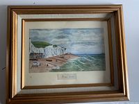 Full view of framed painting showing the coastal scene with Dover white cliffs, beach, and buildings. The painting is surrounded by a white mat inside a gold wood frame.