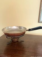 Full profile of the copper warming pan with burner and handle on wooden surface.