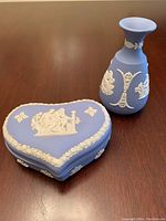 Photo showing the blue jasperware heart-shaped trinket box and vase on a wooden surface, highlighting overall shape and decoration style