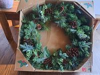 Full view of large artificial wreath with pinecones and greenery in the original box.
