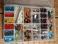 Top-down view of a plastic box with multiple compartments filled with various beads and jewelry making supplies.