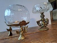 Two decorative crystal glass bowls on brass stands displayed on wooden surface.