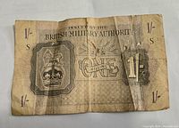 Front side of the WWII British Military Authority one shilling note showing denomination, crest, and issuing authority text with noticeable wear and tear.
