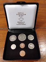 Set of seven Canadian coins displayed inside black velvet holder and black hinged case with satin interior by Royal Canadian Mint.