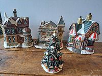 View of all three ceramic Christmas village buildings and decorated tree together on wooden surface