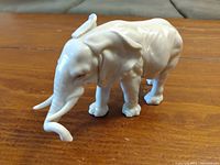 Glossy white ceramic elephant figurine on a wooden surface, showing detailed texture and shape