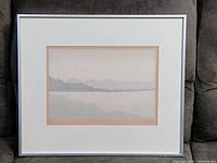 Full view of the framed print showing the metal frame, white matting and the subtle mountain and water landscape artwork.