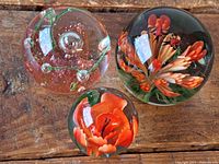 Top view of three glass paperweights with orange themes on wooden surface