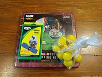 Golf practice kit items displayed together on table showing the box, the Smooth Swing aid, and the yellow balls in plastic bag.
