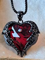 Front view of the heart-shaped pendant with dark red faceted gemstone and black metal with small black stones.