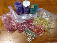Various colors and sizes of holiday bead garlands in bags and tubes on wooden surface