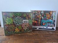 Photo showing two unopened jigsaw puzzle boxes, one with succulents and the other with potting shed image, placed side by side.