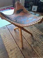 Leather seated stool with triangular seat showing painted rhino and acacia tree design and laced edges.