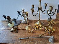View of all candle stick holders arranged on wooden surface including brass and silver-tone holders and a metal candle snuffer.