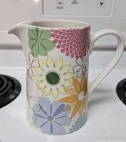 Pitcher with colorful floral Crazy Daisy pattern displayed on a white stove background.