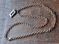 Sterling silver necklace laid out on wooden surface showing chain links and rectangular bone-shaped pendant.