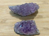 Two amethyst crystal clusters placed on a wood surface, clearly showing crystal structure and varying purple tones.