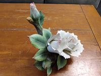 Top view of the ceramic flower sculpture showing white delicate petals and green leaves with a brown stem on a wooden surface.