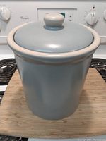Photo of gray ceramic pot with lid on wooden surface in front of stove.