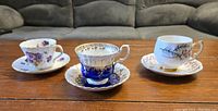 Front view of three bone china teacups with matching saucers, each styled distinctly showing floral and decorative patterns on a wood surface.