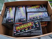 Box showing multiple unopened packages of NOMA Marquee lights stacked inside a cardboard box.
