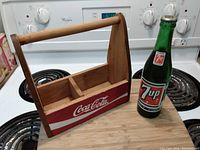 Wooden Coca-Cola branded basket beside vintage green 7Up bottle on a stove top
