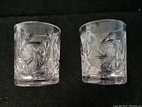 Pair of crystal cut glass tumblers showing pinwheel and star cut designs on a black background.