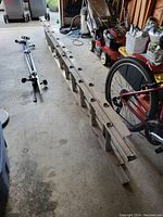 Photo showing the aluminum extension ladder in a garage setting alongside other garden and bicycle equipment. Ladder is folded in a retracted state, showing its aluminum structure and rungs.