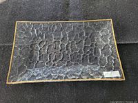 Rectangular clear glass plate with textured surface and gold colored trim on edges laid on black fabric.