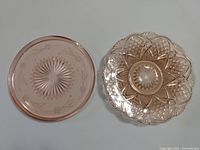 Top-down view of two pink glass serving plates side by side, showing etched floral and geometric designs.