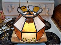 Front view of hanging stained glass light fixture showing floral design panel with white flowers and green leaves, amber and white glass sections.