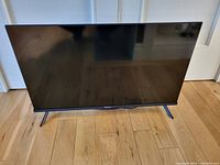 Front view of the Hisense 32" LED LCD TV showing the screen and stand on wooden floor.