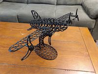 Black metal airplane sculpture on wooden table with a grey couch in the background, showing side angle and open ring design.