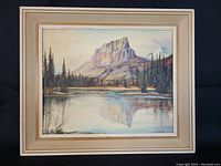 Front view of the oil painting depicting Mount Eisenhower with its reflection on water, surrounded by pine trees, in a wooden frame.