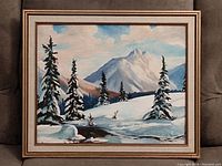 Framed painting showing a winter mountain landscape with pine trees and a stream