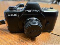Front view of Pentax Auto 110 camera showing branding and attached 24mm f/2.8 lens with lens cap.