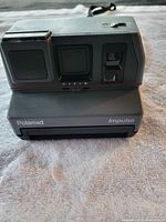 Front view of black Polaroid Impulse camera, showing lens, viewfinder, and front panel markings