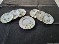 Set of seven Royal Albert plates with white dogwood floral design arranged on black surface, showing six smaller plates and one larger scalloped plate.