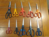 Top-down photo showing 10 scissors with varied handle colors and sizes on a wooden surface.