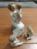 All three Willow Tree 'Grandmother' figurines showing the seated grandmother holding a child and two smaller seated child figures on wood surface.