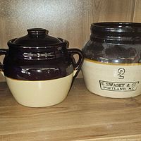 Two ceramic bean pots, one with fitted lid and one open pot with brand and size markings on front.