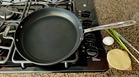 Photo of the All-Clad 12-inch frying pan on a gas stove, showing the non-stick interior and stainless steel handle.