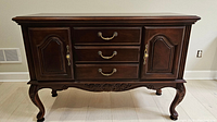 Full front view of the stained dark brown sideboard showing three drawers in center, cabinet doors on either side, carved front legs and antiqued brass hardware.