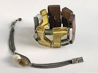 Two bracelets: one chunky geometric elastic bracelet with yellow-green glass and wood components, pewter tag visible; the other a multi-strand chain bracelet with glass beads and toggle clasp.