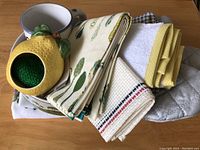 Top view showing ceramic lemon scrubber holder with green kitchen sponge inside, oversized mug, and folded dish towels and hand towels with vegetable and striped patterns
